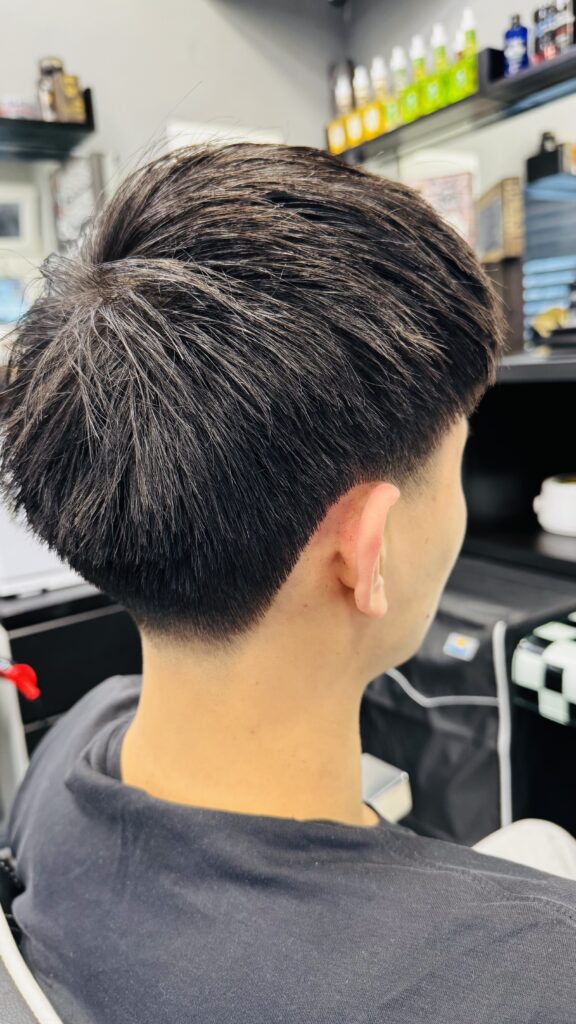 Moderner Fade-HaarschnittDieser Haarschnitt kombiniert eine klare Linienführung mit einem weichen Übergang. Die Seiten und der Nackenbereich sind präzise mit einem sauberen Low Fade ausrasiert, der einen natürlichen Verlauf zur Fülle am Oberkopf schafft. Das Deckhaar bleibt bewusst länger und voluminös, wodurch vielseitige Styling-Möglichkeiten entstehen – von lässig natürlich bis strukturiert gestylt. Ein Schnitt, der gepflegt wirkt und gleichzeitig modern und jugendlich aussieht.